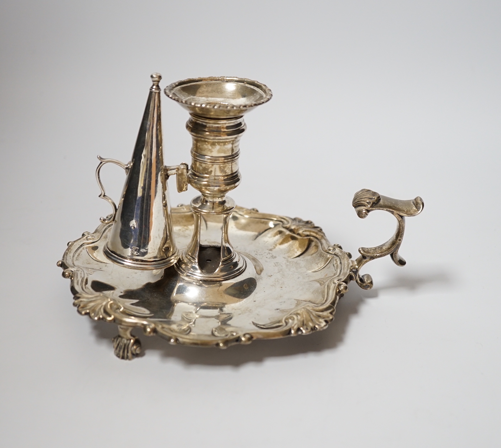 A George II silver chamberstick, with shell border, on three scroll feet, William Grundy, London, 1756, with extinguisher(marks rubbed), overall 18.5cm, 14.1oz.